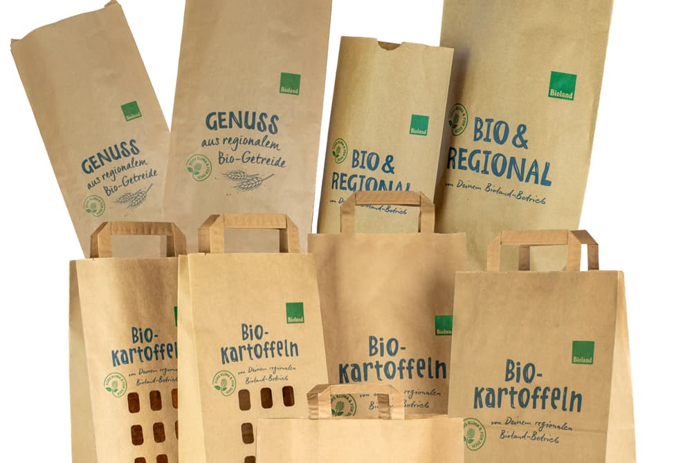 Verschiedene braune und weiße Papiertüten mit den Aufschriften „Bio & Regional“ und „Bio-Kartoffeln“, mit Griffen und umweltfreundlichen Symbolen.