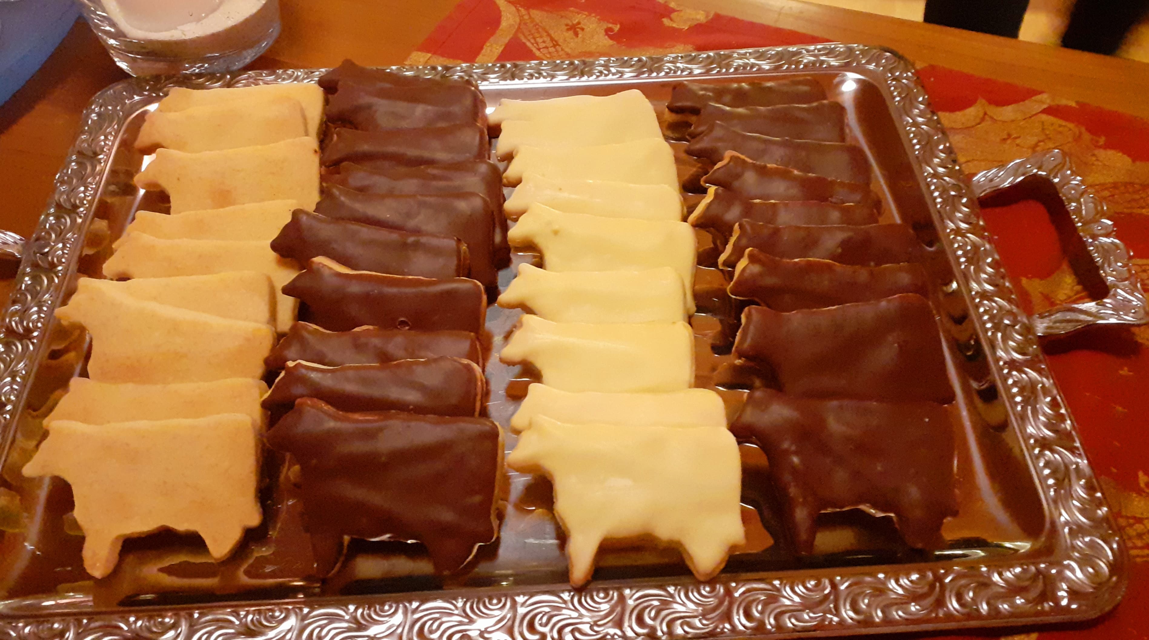 A silver tray holding cow-shaped cookies, featuring rows with chocolate, white, and plain flavors, arranged on a red tablecloth.