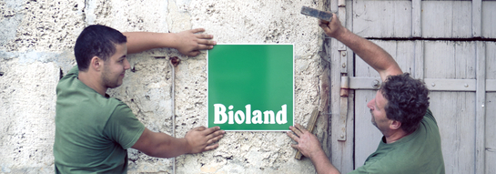 Zwei Männer bringen Bioland-Schild an Wand an