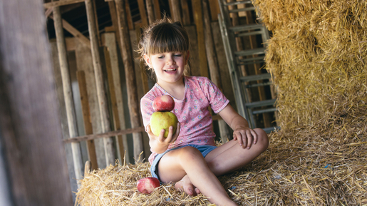 Ein Mädchen hält einen Bioland-Apfel in der Hand und sitzt auf einem Heuballen