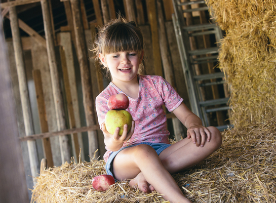Ein Mädchen hält einen Bioland-Apfel in der Hand und sitzt auf einem Heuballen
