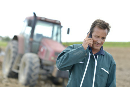 Landwirt telefoniert auf Feld vor Traktor