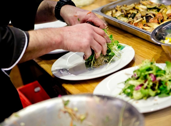 Koch richtet Bio-Salat auf einem Teller an