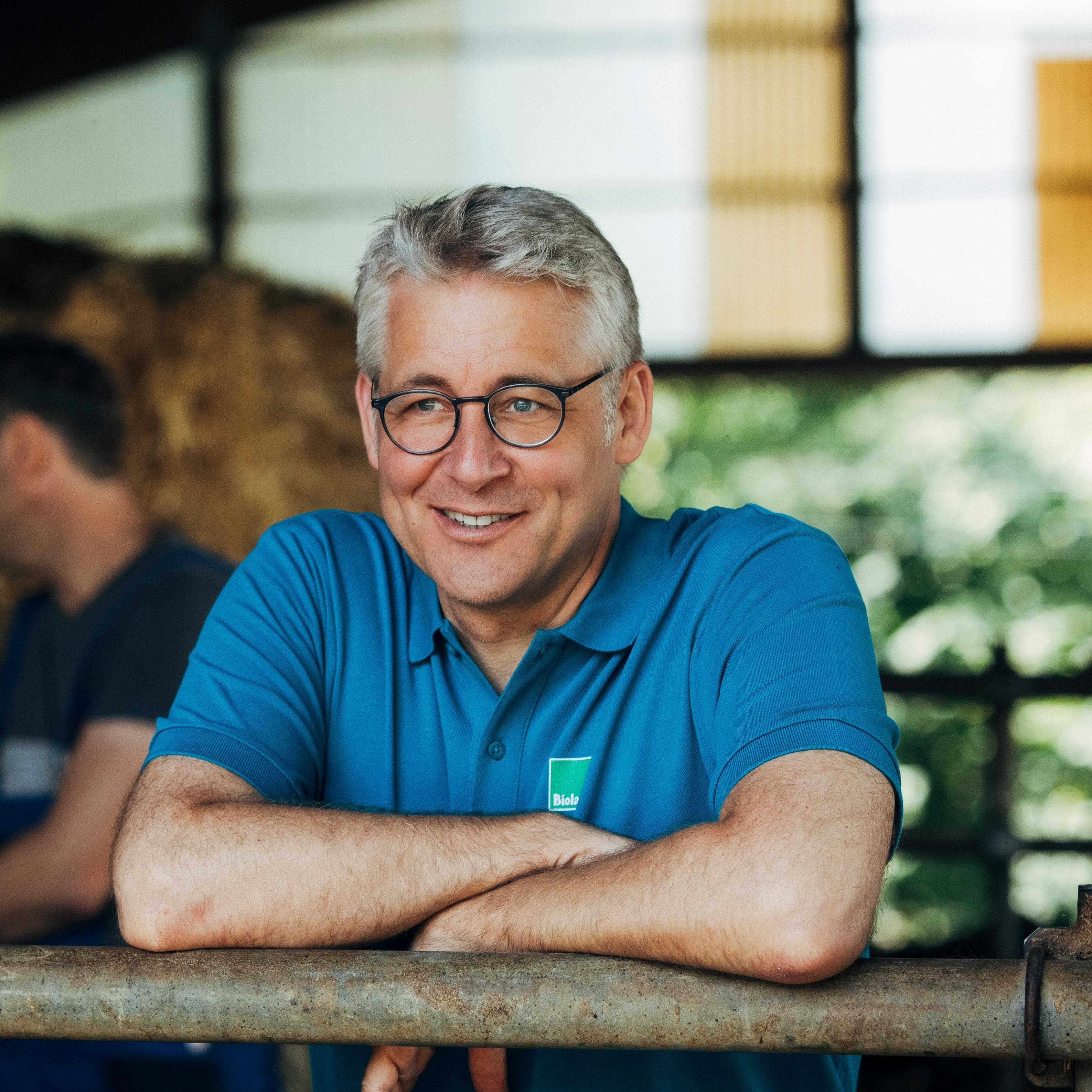 Bioland-Präsident Jan Plagge, mit einem blauen Polohemd, lehnt sich in einer sonnendurchfluteten Innenumgebung an ein Geländer.